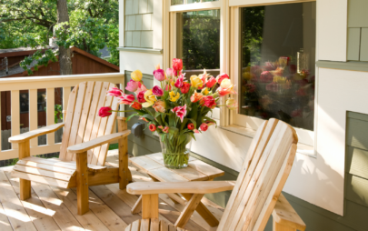 two teak lounge chairs on front porch with vase of pink and yellow flowers on the table between them