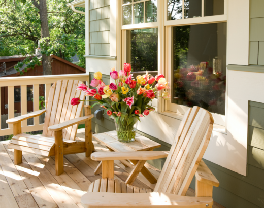 two teak lounge chairs on front porch with vase of pink and yellow flowers on the table between them