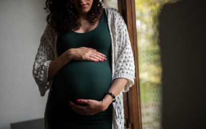Pregnant woman wearing a green dress and cradling her belly