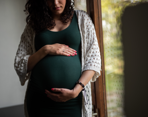 Pregnant woman wearing a green dress and cradling her belly