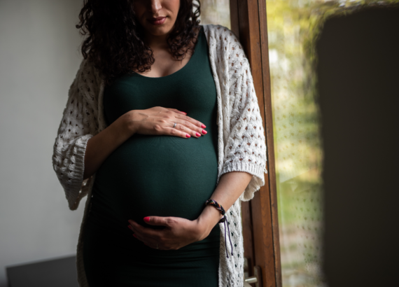 Pregnant woman wearing a green dress and cradling her belly