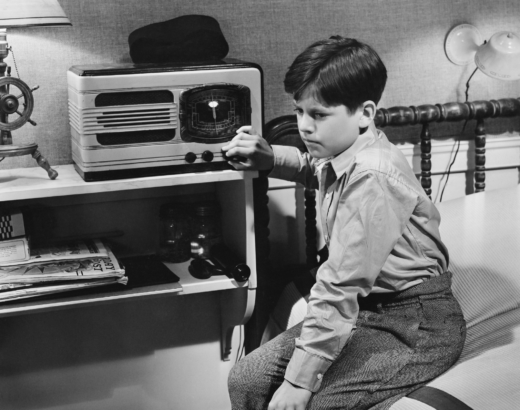 black and white photo of a boy sitting on his bed listening to the radio