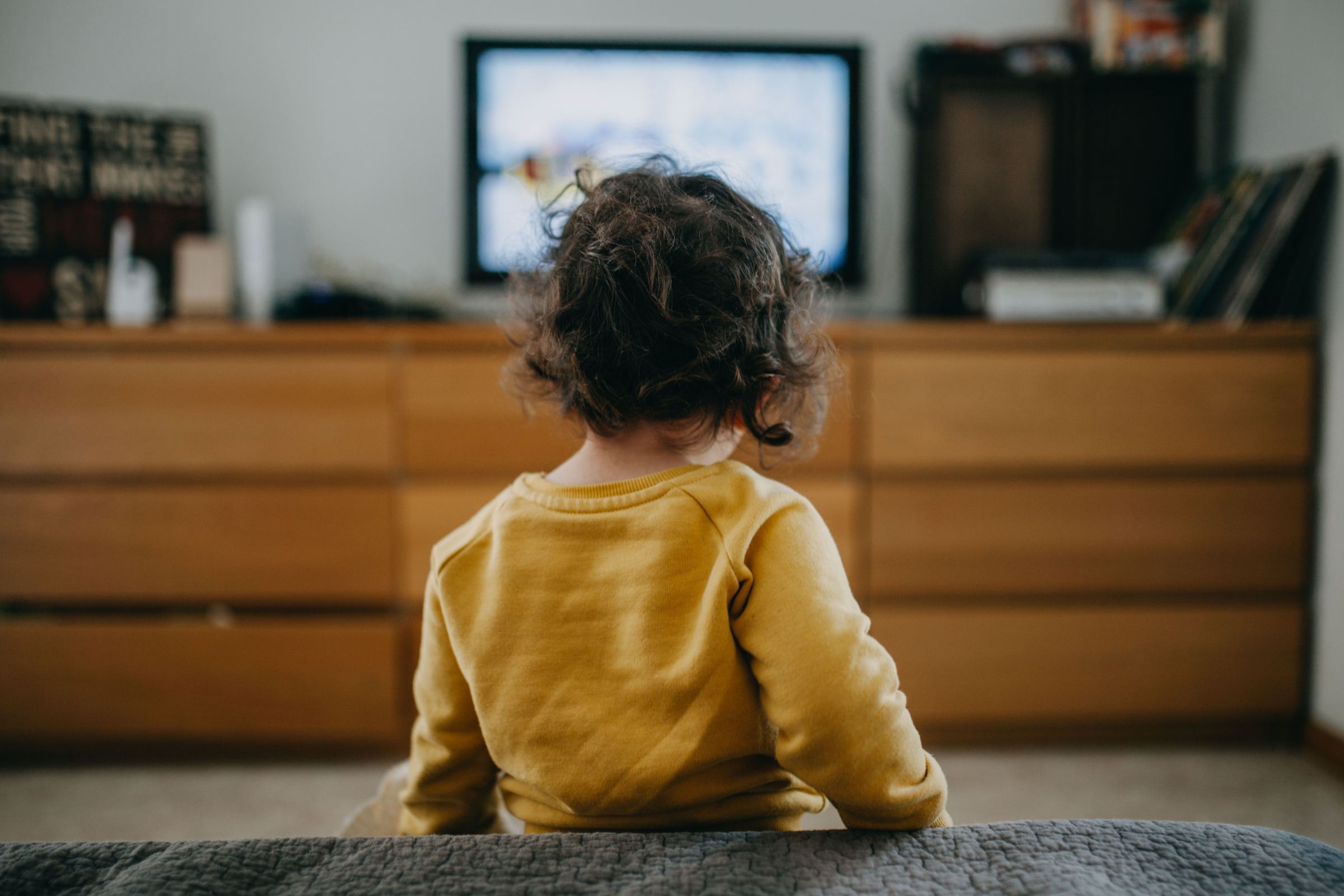 toddler wearing yellow staring at a tv screen