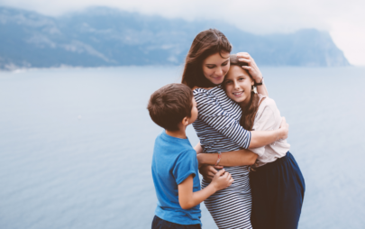 woman hugging her daughter and son against the background of a lake