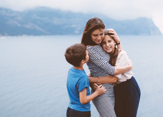 woman hugging her daughter and son against the background of a lake
