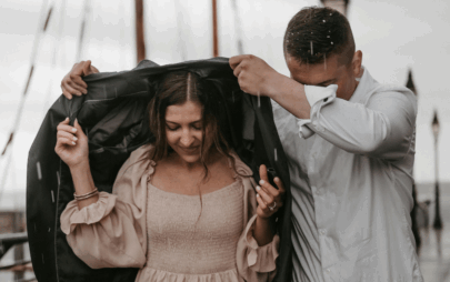 A man holding his coat over a woman's head as it rains to keep her dry