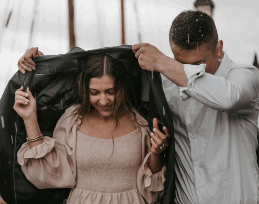 A man holding his coat over a woman's head as it rains to keep her dry