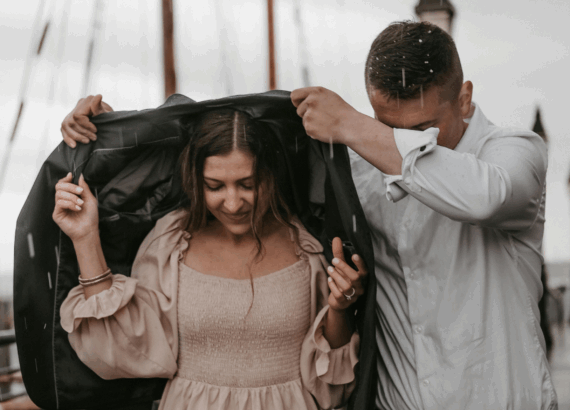 A man holding his coat over a woman's head as it rains to keep her dry