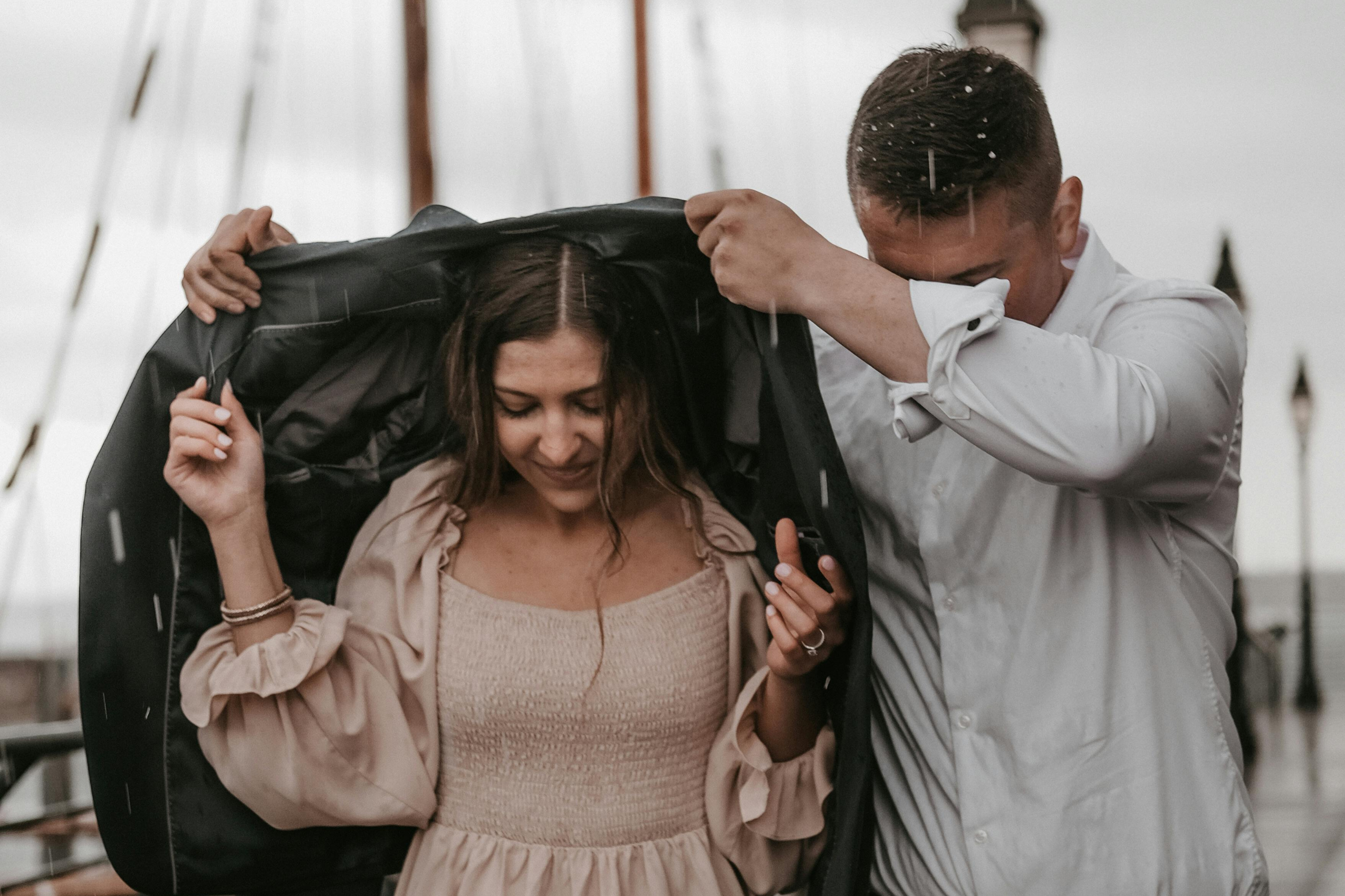 A man holding his coat over a woman's head as it rains to keep her dry