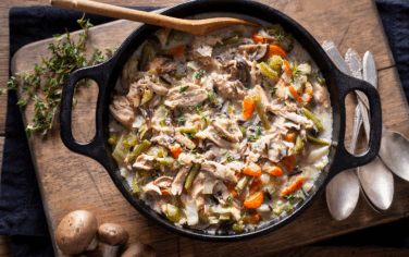 soup with chicken and vegetables in a large cast iron pot surrounded by spoons and herbs