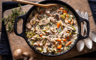 soup with chicken and vegetables in a large cast iron pot surrounded by spoons and herbs