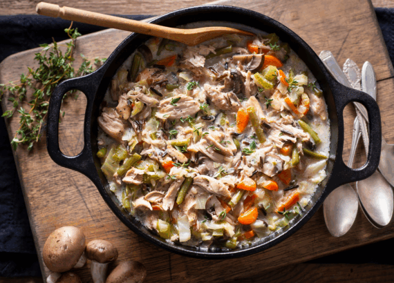 soup with chicken and vegetables in a large cast iron pot surrounded by spoons and herbs