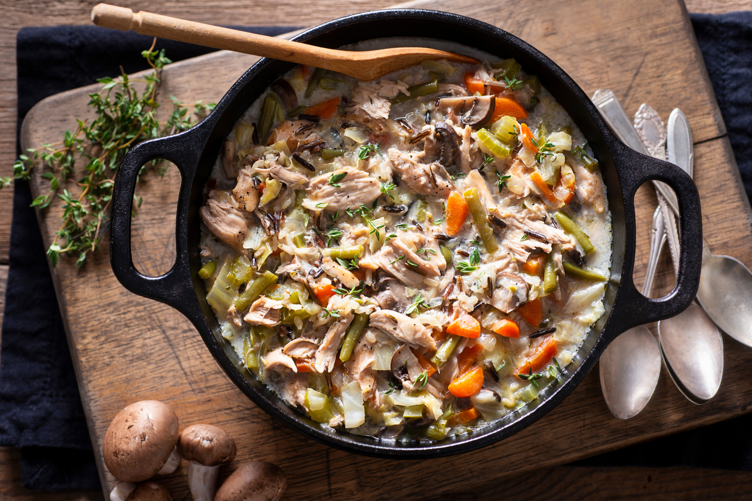 soup with chicken and vegetables in a large cast iron pot surrounded by spoons and herbs