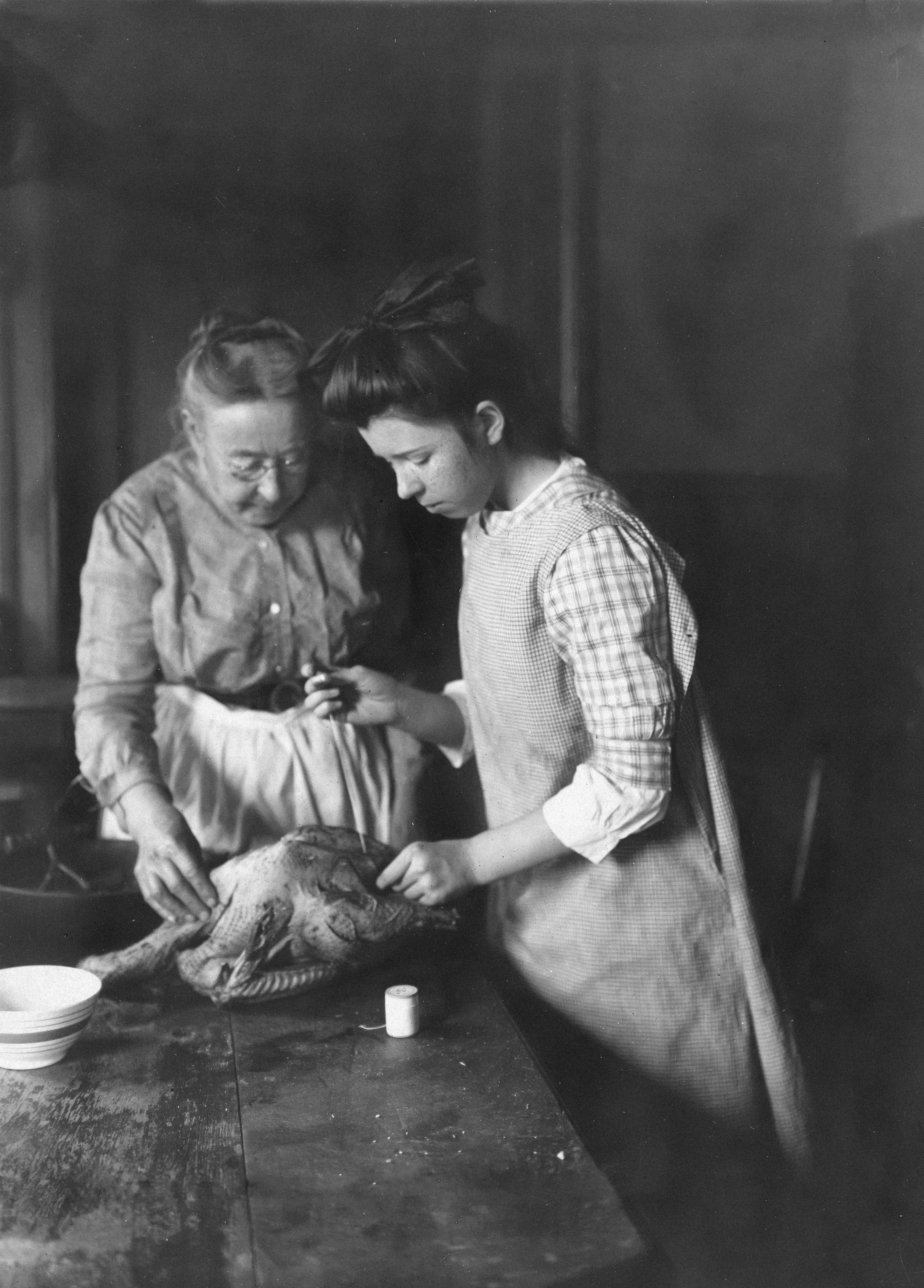older woman helping a younger woman dress a chicken for roasting